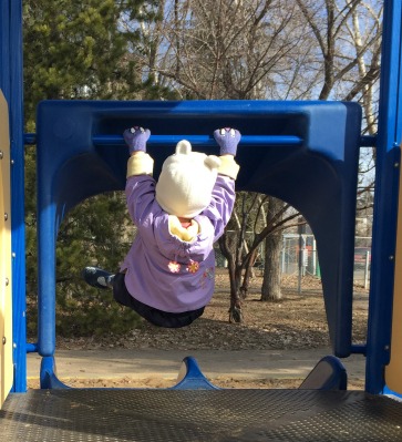 Little girl hangs from bar at playground