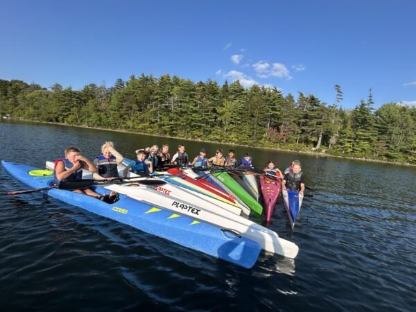 A group of youth gathered together in kayaks on a lake for Saskawa Summer Camp