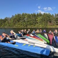 A group of youth gathered together in kayaks on a lake for Saskawa Summer Camp