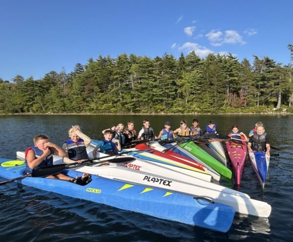 A group of youth gathered together in kayaks on a lake for Saskawa Summer Camp