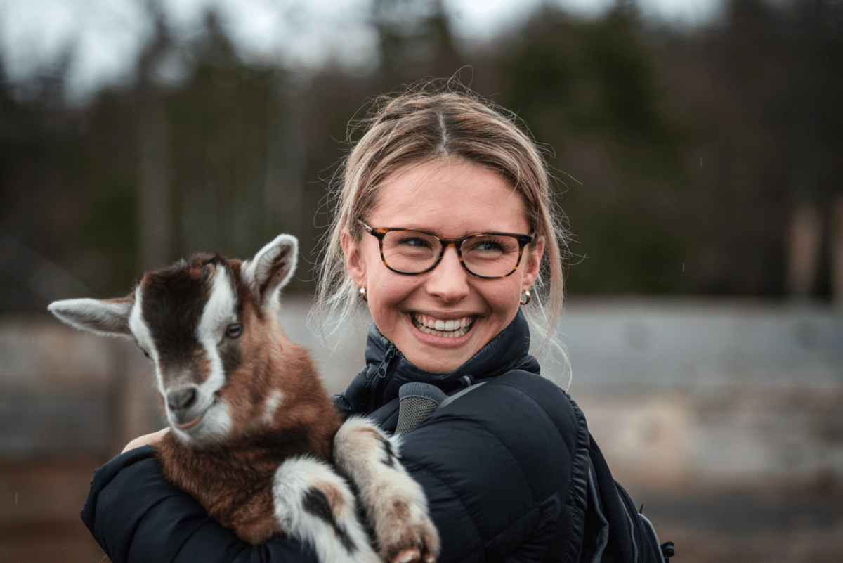 Young woman smiling holding an Alpine goat at Ataraxy Farm on Eastern Shore Escape Tour from Settled Nomads