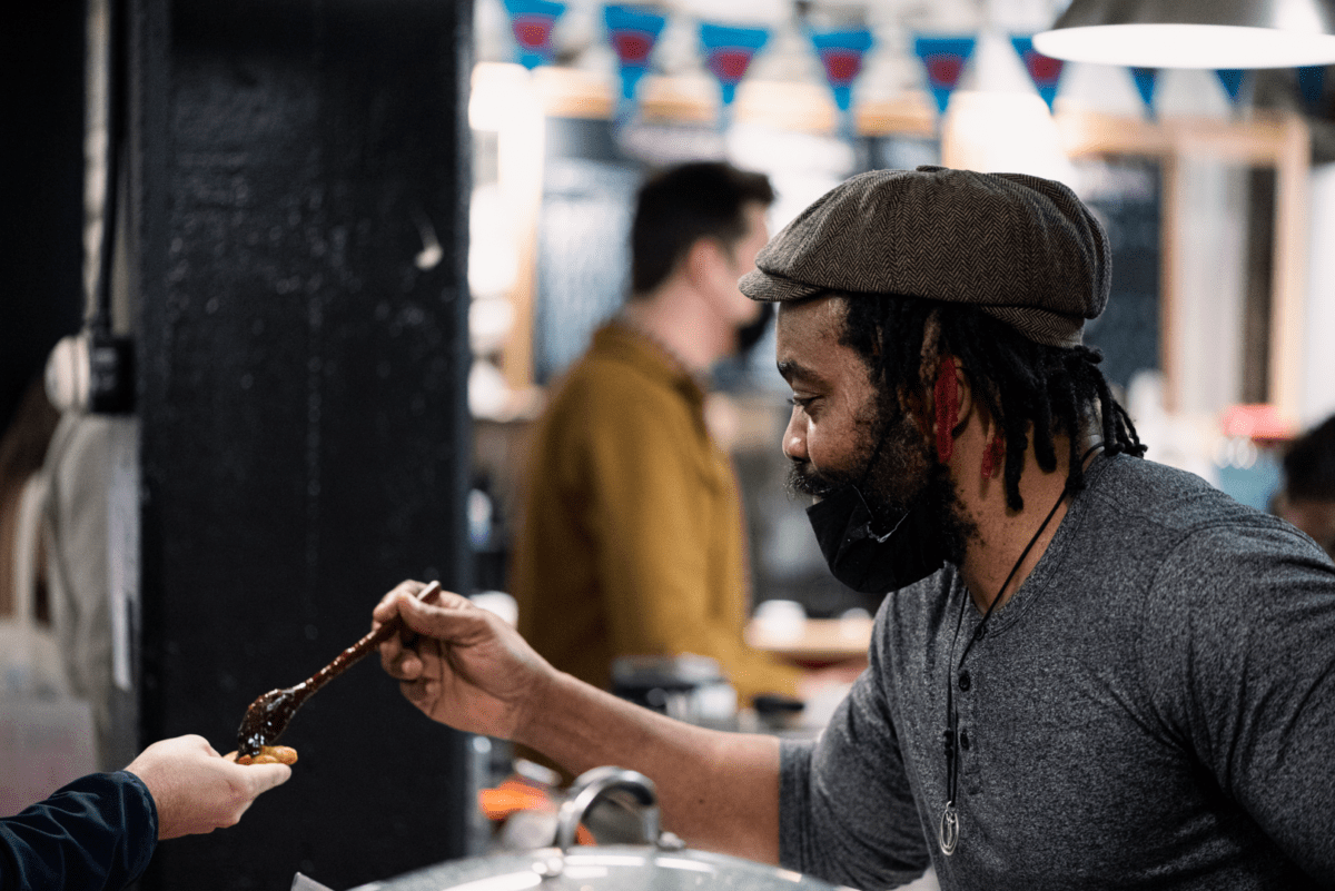 Um homem oferece a um cliente uma amostra de geleia ou chutney no Halifax Brewery Market, primeira parada do Settled Nomads Tour na costa leste da Nova Escócia