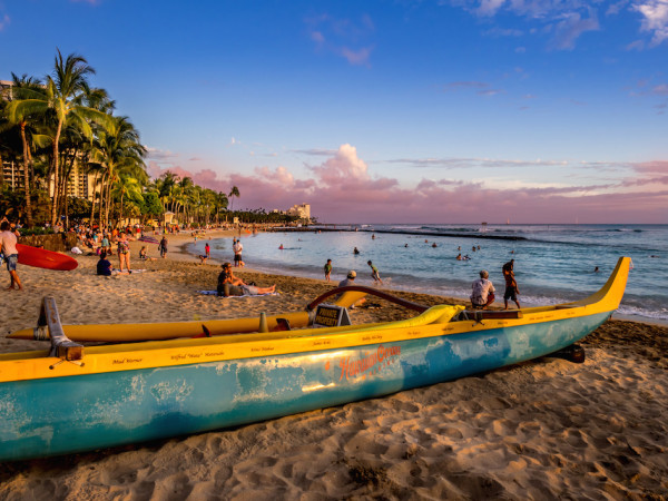 Tourists on the beach front at sunset on Waikiki beach in Oahu. Waikiki beach is beachfront neighborhood of Honolulu, best known for white sand and surfing.