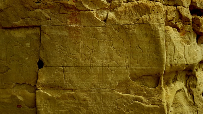 These are some of the earliest petroglyphs at Writing on Stone, dated from before the time guns and horses arrived on the Prairies, as evidenced by the circular shields. These shields fell out of use after the advent of guns as they no longer offered adequate protection.