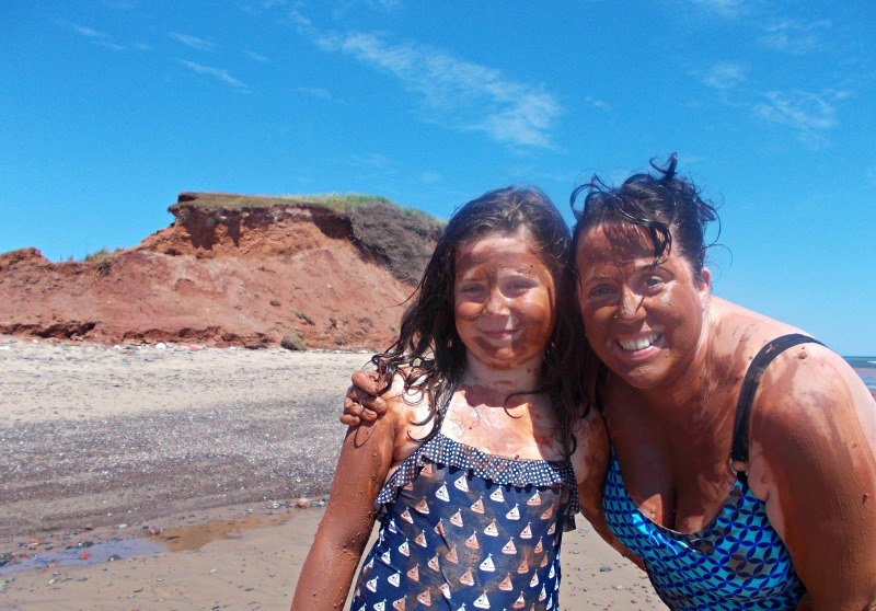 A escritora de viagens Helen Earley e sua filha Lucy tomando banho de lama em La Salicorne - Um passeio de caiaque pelas águas calmas e rasas de Bassin aux Huitres (Oyster Bay) nos leva às falésias vermelhas da Ilha Boudreau, onde rejuvenescemos um espesso banho de lama de argila vermelha.