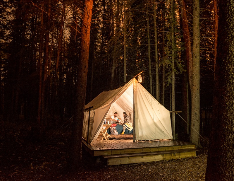 游客们在他们照明的梅蒂斯捕兽人帐篷里闲逛，同时露营过夜。 落基山庄国家历史遗址。 Credit Parks Canada - Scott Munn