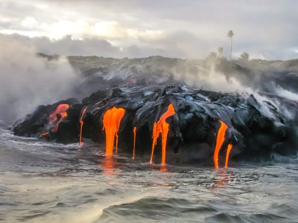 美国夏威夷大岛基拉韦厄火山的海景。 一座从 1983 年开始营业的不安定火山。拍摄于日落时分，熔岩在黑暗中发光，跳入大海。