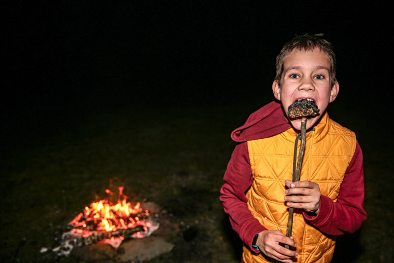 menino comendo s'mores ao redor da fogueira